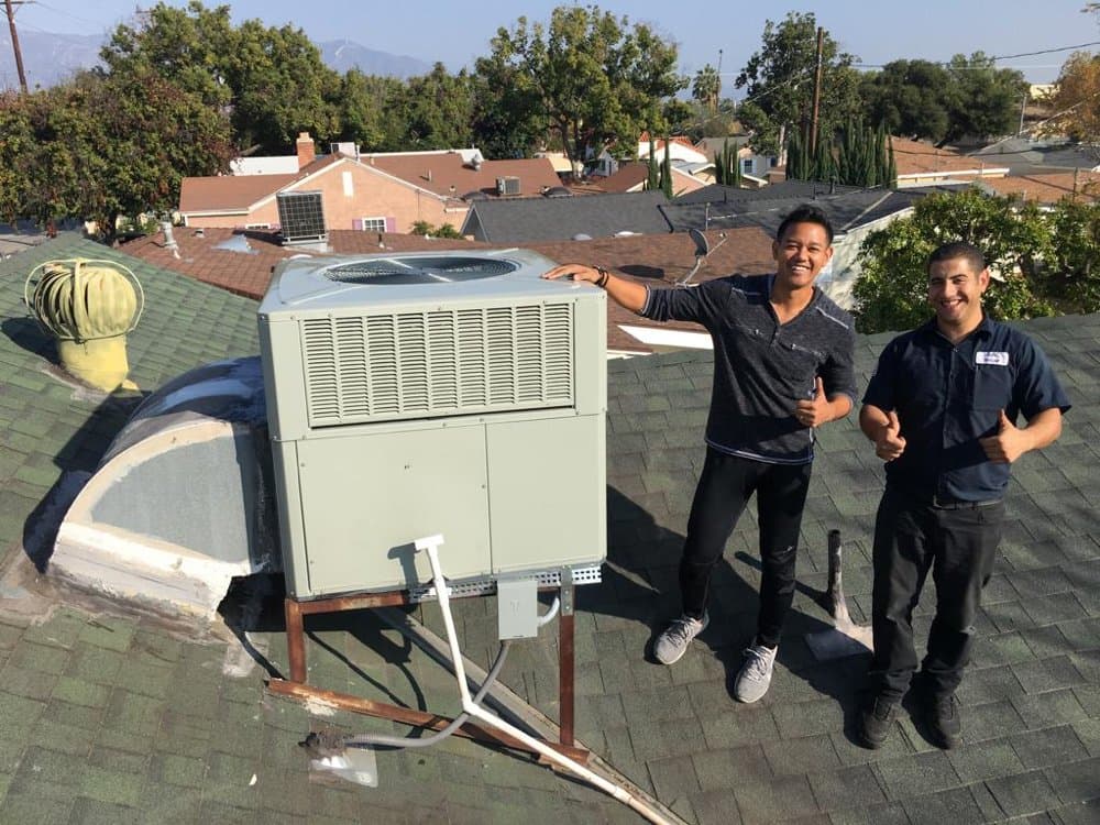 Two NextGen technicians on a roof beside a freshly installed unit, both smiling